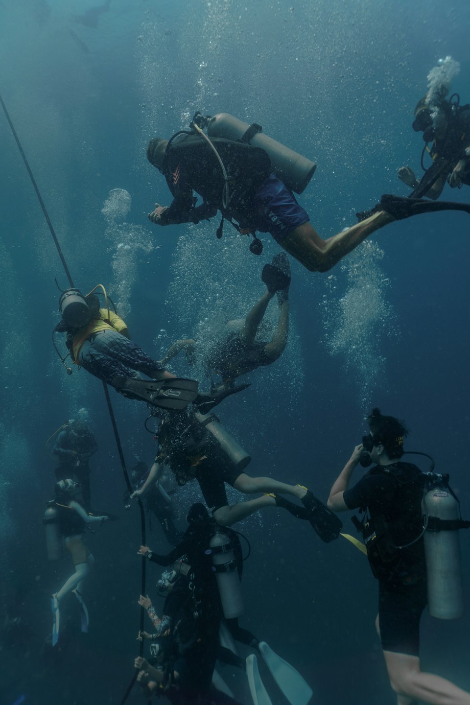 Penyelam scuba berenang di bawah air sambil berpegangan pada tali vertikal.